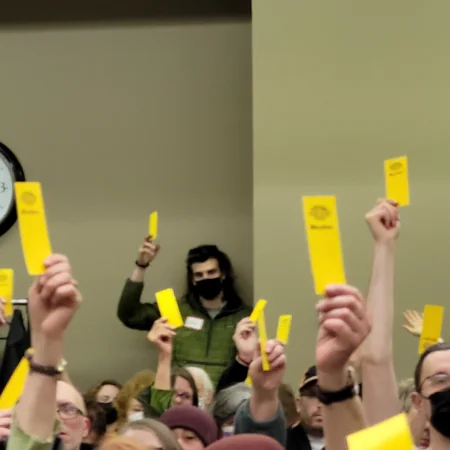 A group of Steep Hill Food Co-op members holding up their yellow voting cards at a special community meeting.