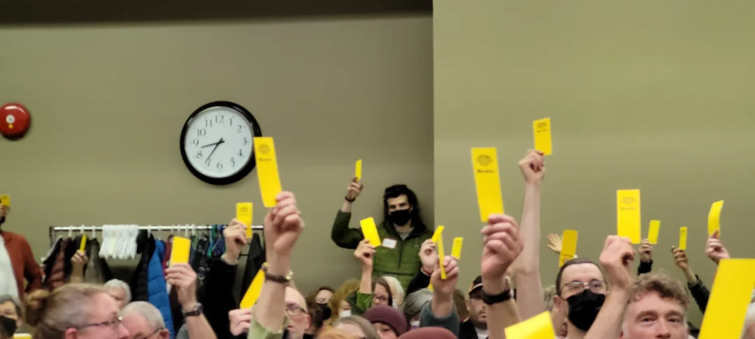 A group of Steep Hill Food Co-op members holding up their yellow voting cards at a special community meeting.