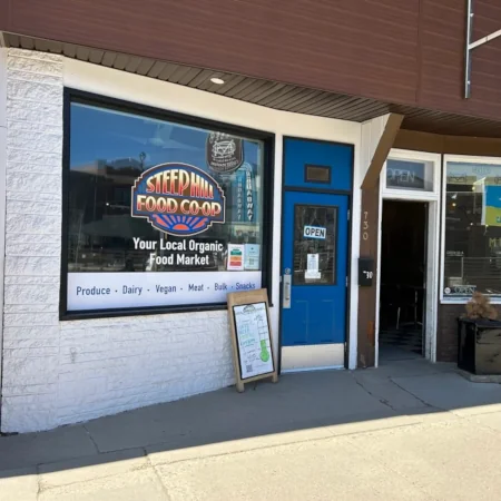 The store front of Steep Hill Food Co-op with largely visible vinyl window sign of the Steep Hill logo with text that reads, Your Local Organic Food Market.