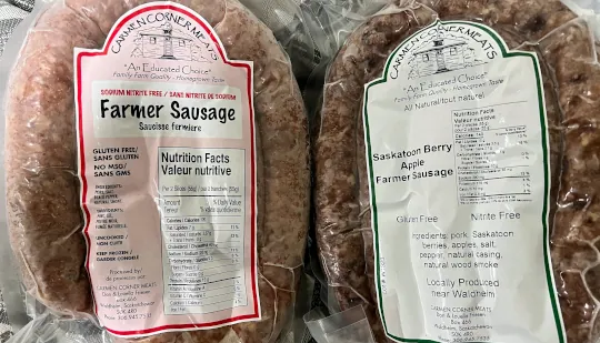 Two Carmen Corner Meat sausage packages are laid out side-by-side, Farmer Sausage and Saskatoon Berry Apple.