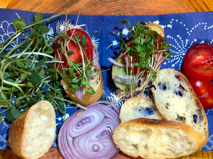 A few slices of bread laying on a surface with tomato and micro-greens on top.