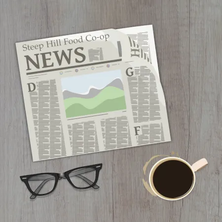 A wooden kitchen table with a Steep Hill Food Co-op news paper, reading glasses and a cup of coffee sitting on it.