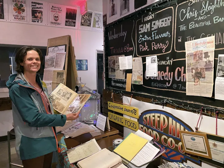 Pam smiling as she holds a photo album next to a table full of history and memorabilia on display at the Steep Hill's 45th Anniversary celebration hosted at Amigos Cantina.