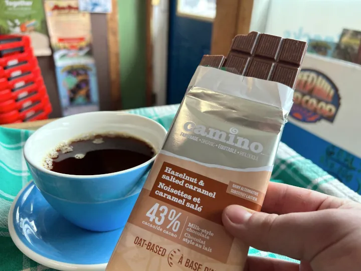 A fresh cup of Museo Coffee in a white and blue cup and saucer along with a Camino hazelnut and slated caramel chocolate bar.