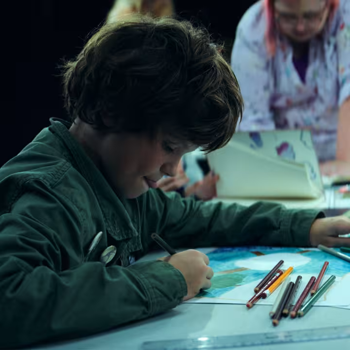 A child sitting at a table colouring with deep concentration.