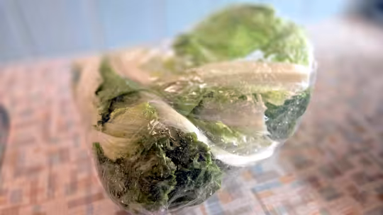 A closeup view of lettuce leaves in a plastic bag sitting on a counter top.