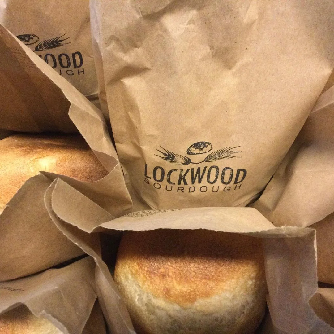 Several brown paper bags with fresh sourdough bread in each bag.