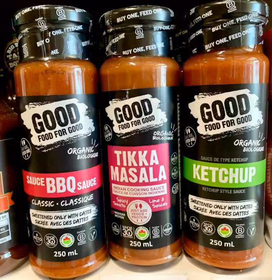 A close up view of three bottles of Good Food For Good lined up side-by-side of BBQ sauce, tikka masala sauce, and ketchup.