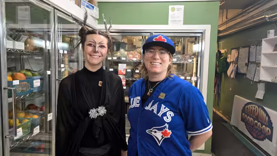 Paige and Amielle posing in halloween costumes next to the coolers at Steep Hill Food Co-op.
