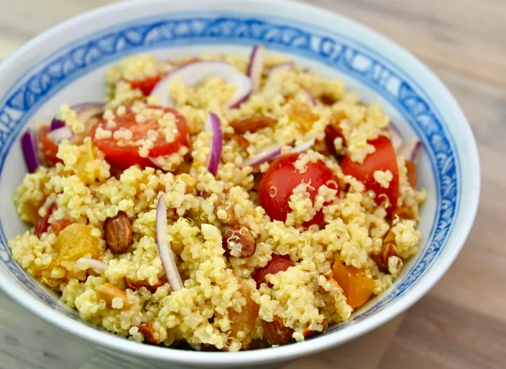 A white bowl with an inner decorative blue trim that has a colourful Quinoa Salad with Apricots and Roasted Almonds.
