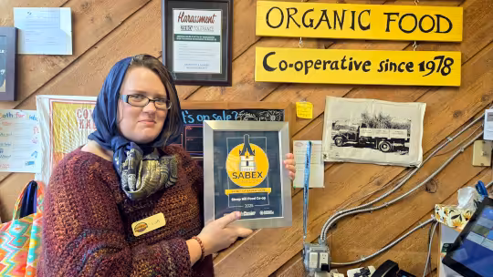 Sol in a granny halloween costume standing next to the Steep Hill till while holding the Sabex finalist award.