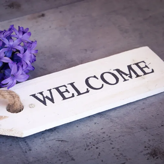 A white wooden sign that says welcome with a purple flower off to the side.