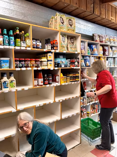 Two people cleaning wooden shelves while one person is looking towards the camera.
