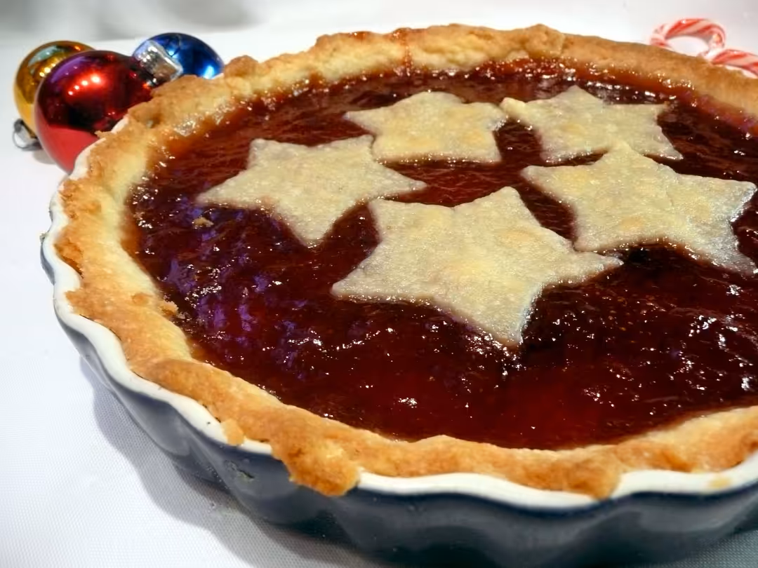 A white ceramic pie plate full of a Jam Tart pie topped with pastry stars and nice golden brown pasty edging.