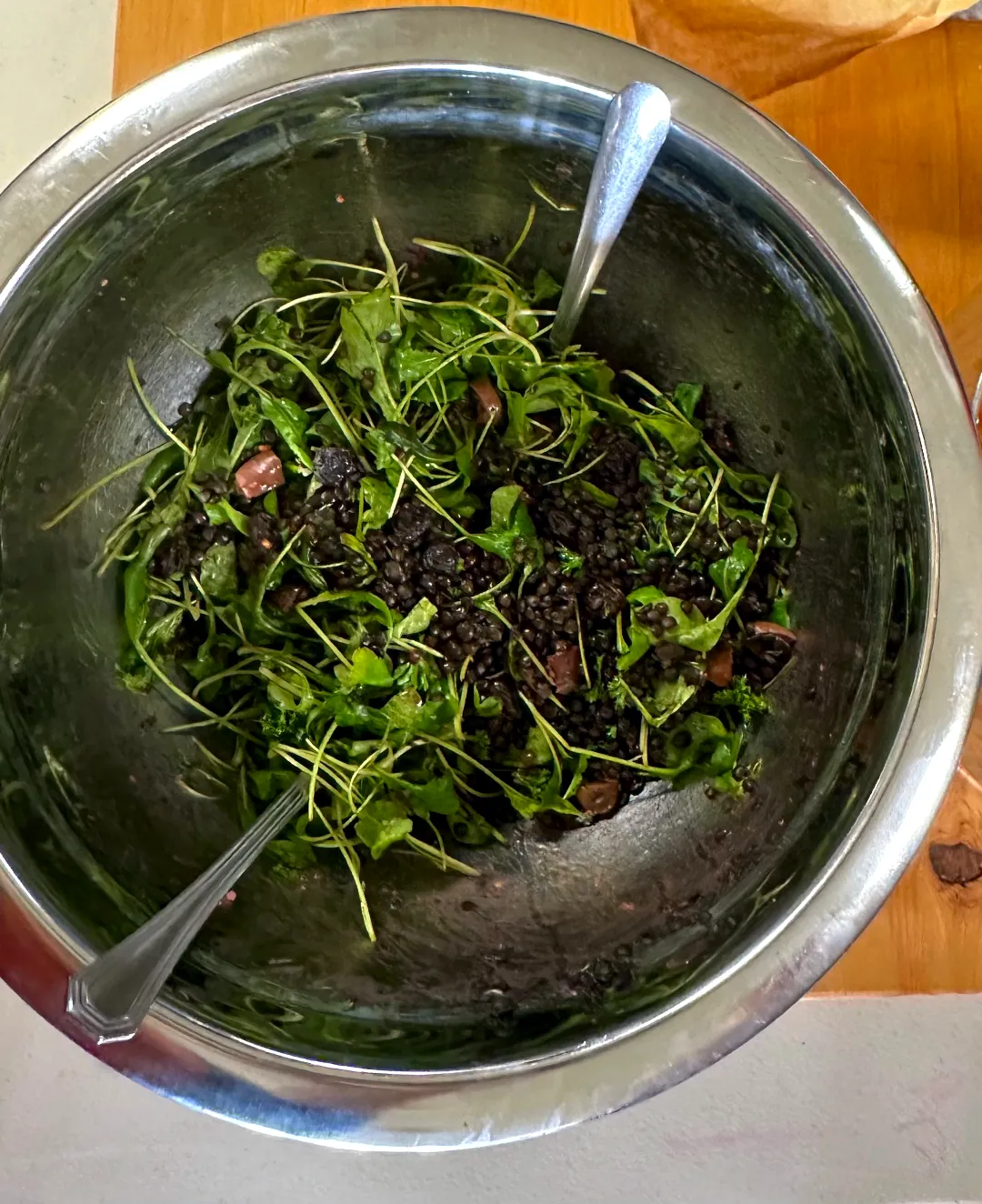 A stainless steel bowl with two utensils pushed into the Lentil Salad.