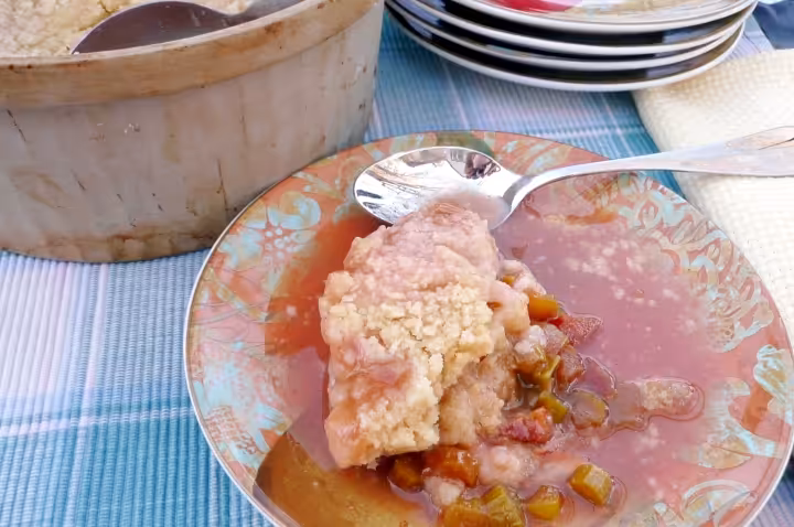 A plate sitting on a table with a table spoon placed beside a portion of rhubarb pudding.