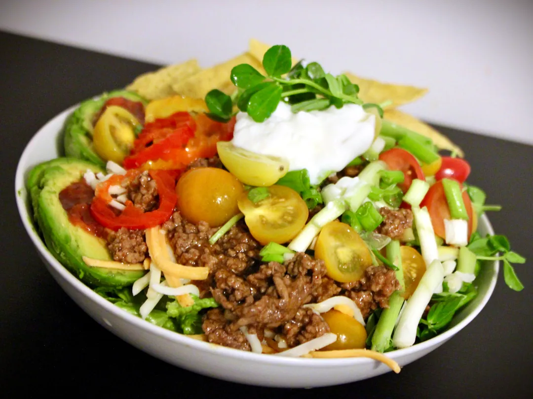 A white bowl sitting on a surface heaping full of a colourful fresh Taco Salad with pea shoots.