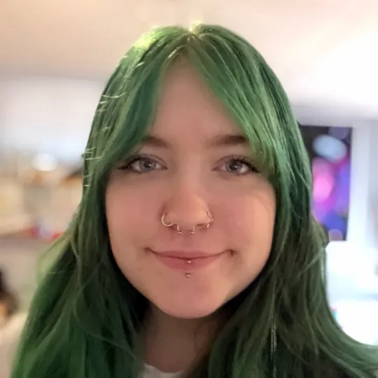 A portrait of staff member Brooklyn smiling with green hair and blue eyes.